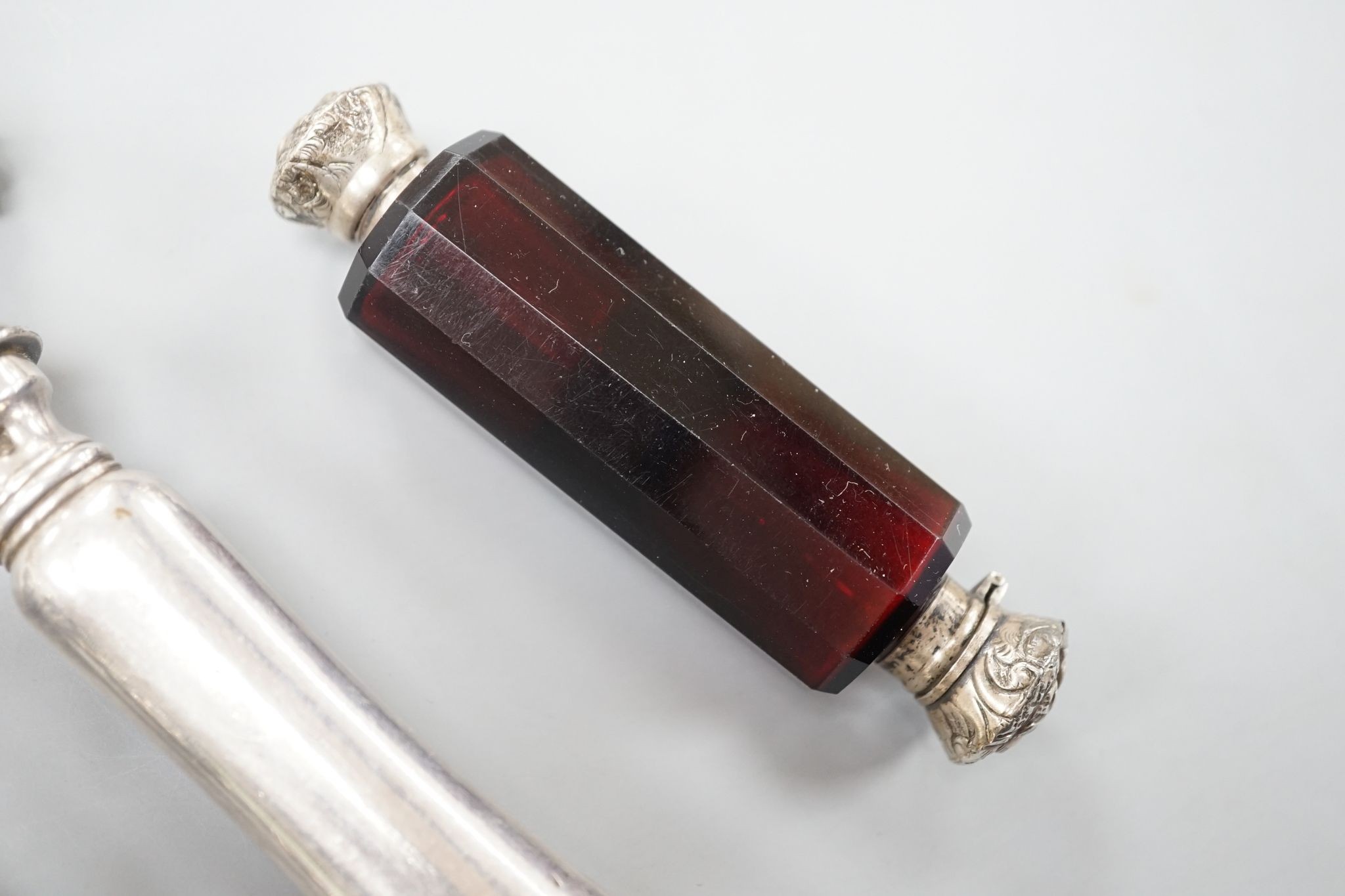 A silver mounted rattle, a white metal mounted double ended ruby glass cent bottle and a silver plated handled roast joint holder.